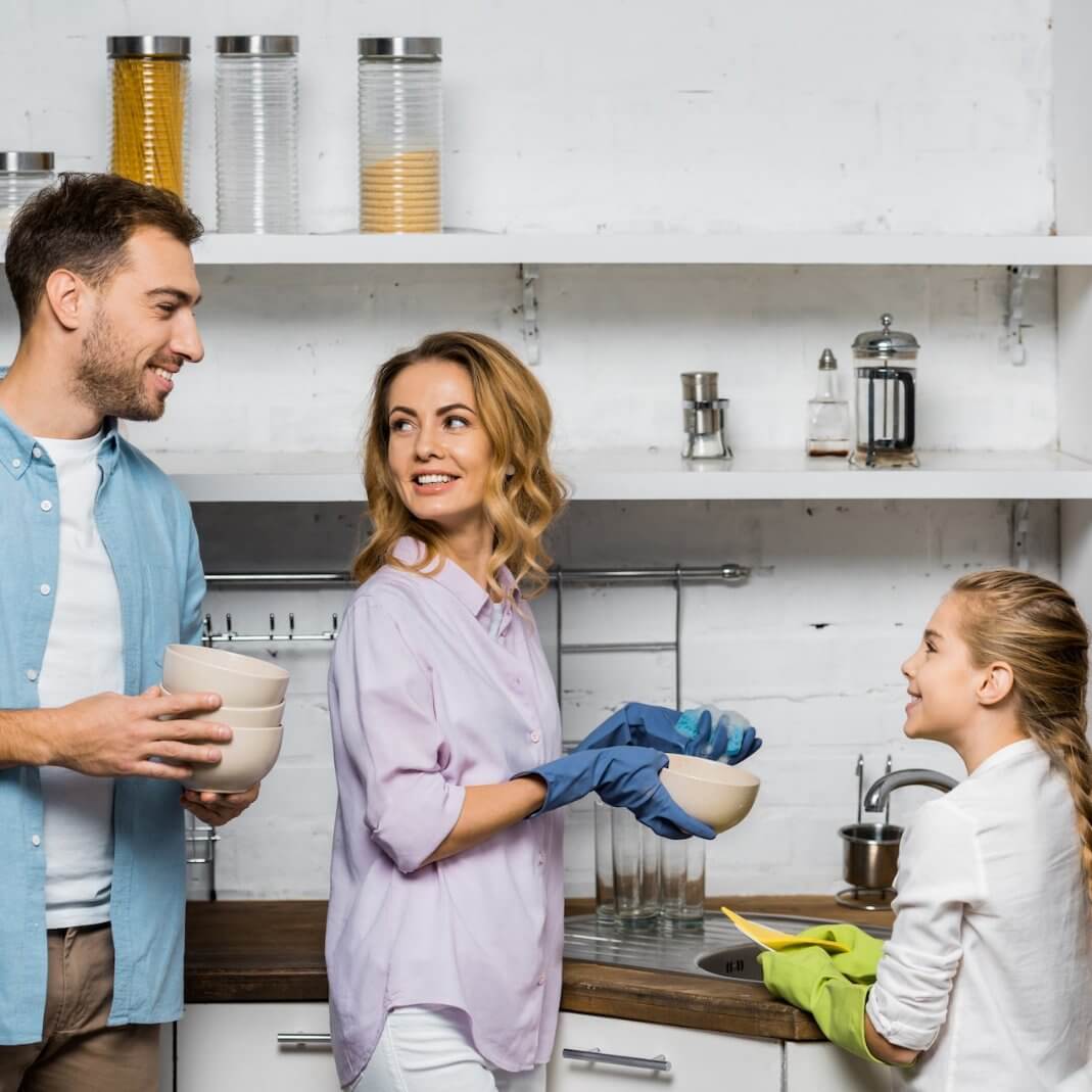 A family happily cleaning together in the kitchen, using multi-purpose cleaners for a sparkling home.