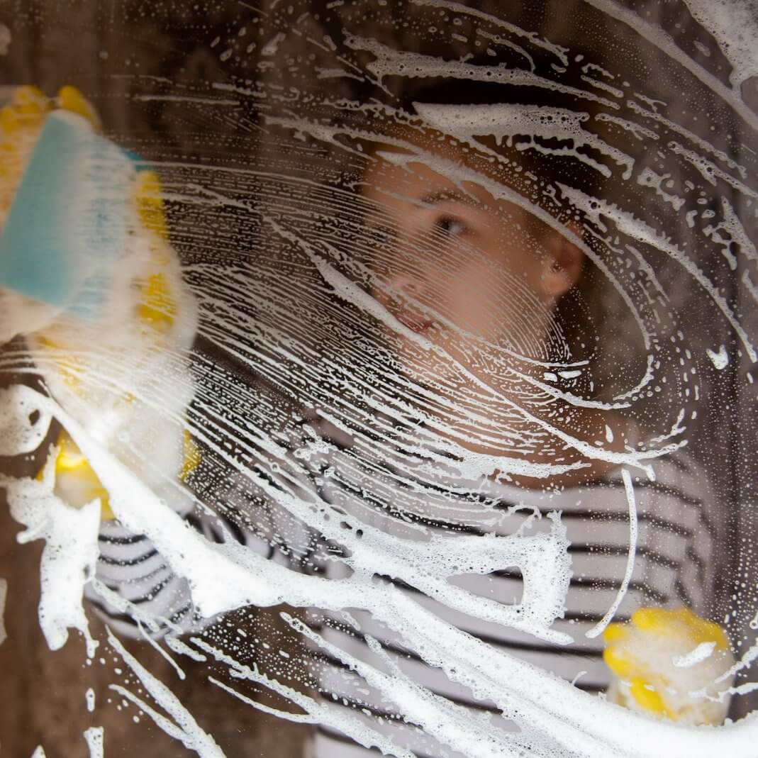 Person cleaning a glass surface with a sponge and cleaner for streak-free shine.