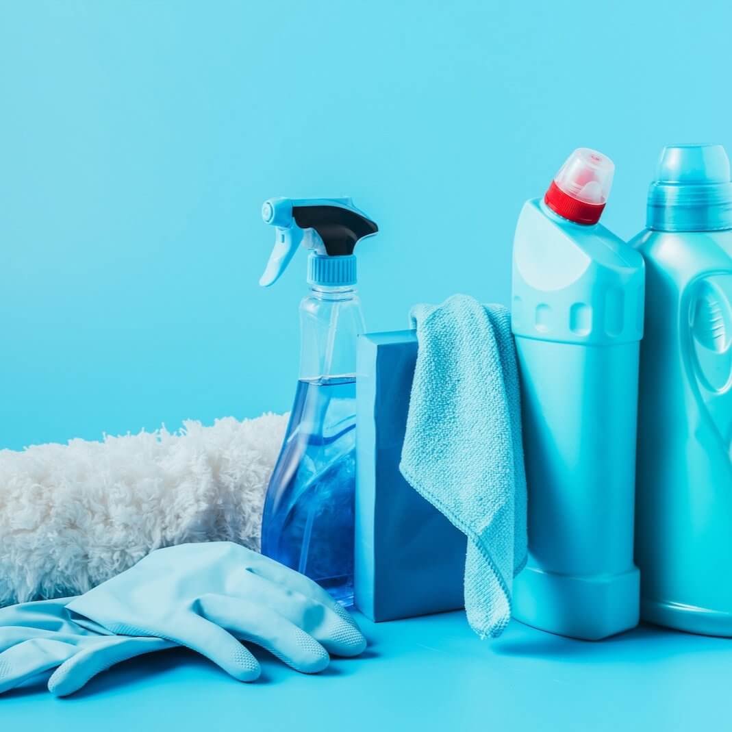 Premium cleaning supplies including spray bottle, gloves, and cleaning solutions on a blue background.
