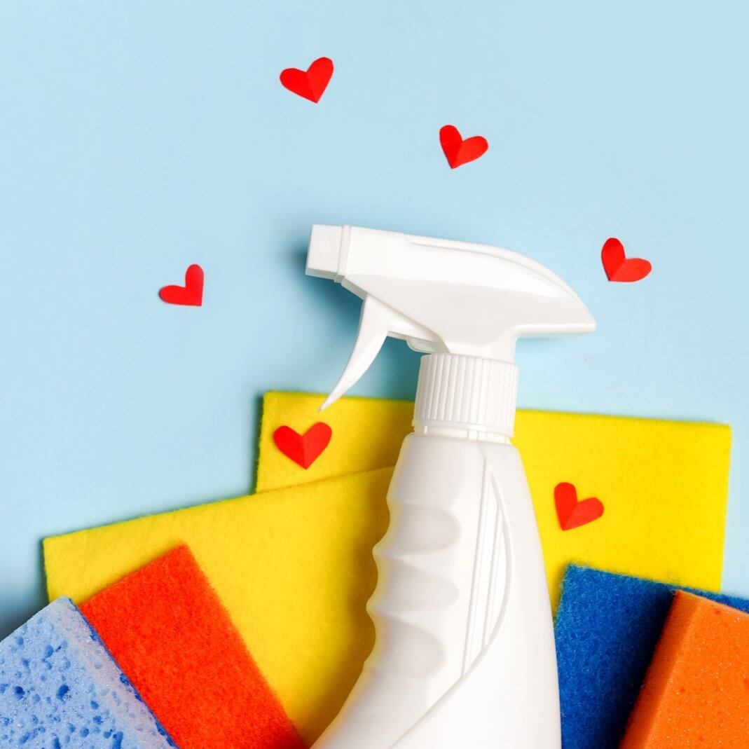 White spray bottle surrounded by colorful sponges and heart shapes, symbolizing effective cleaning solutions.