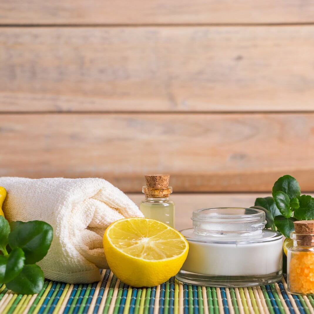 Aromatherapy essentials: lemon, candles, essential oils, and towel on a colorful mat for a soothing cleaning experience.