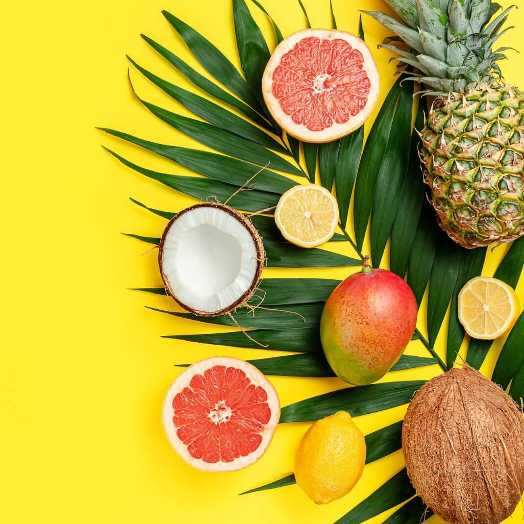 Vibrant tropical fruits and green palm leaves on a bright yellow background, evoking a cheerful paradise vibe.
