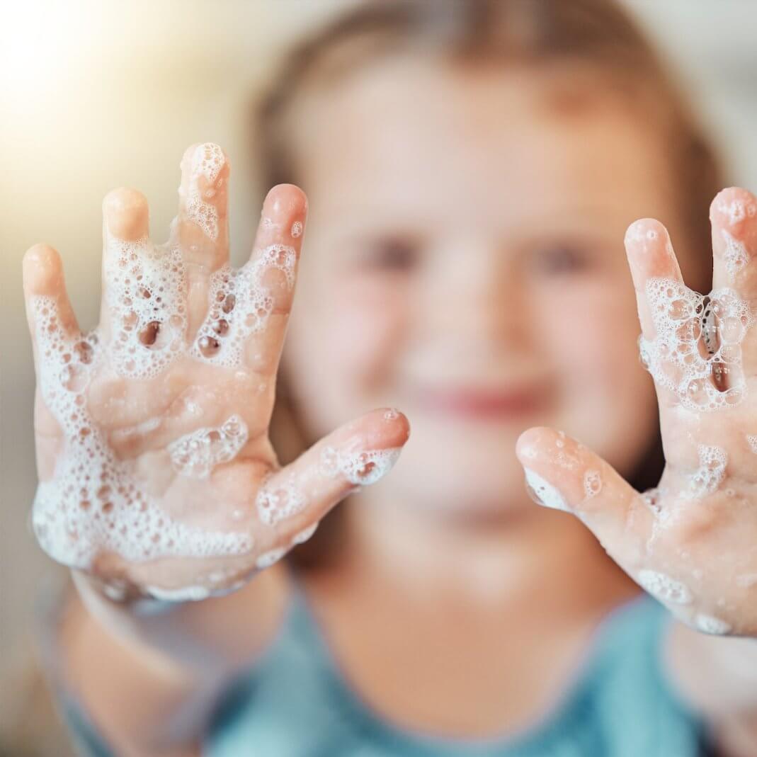 Child with soapy hands smiling, enjoying a luxurious hand washing experience with premium hand soap.